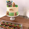 A tiered birthday cake decorated with capybara animal figures and greenery.