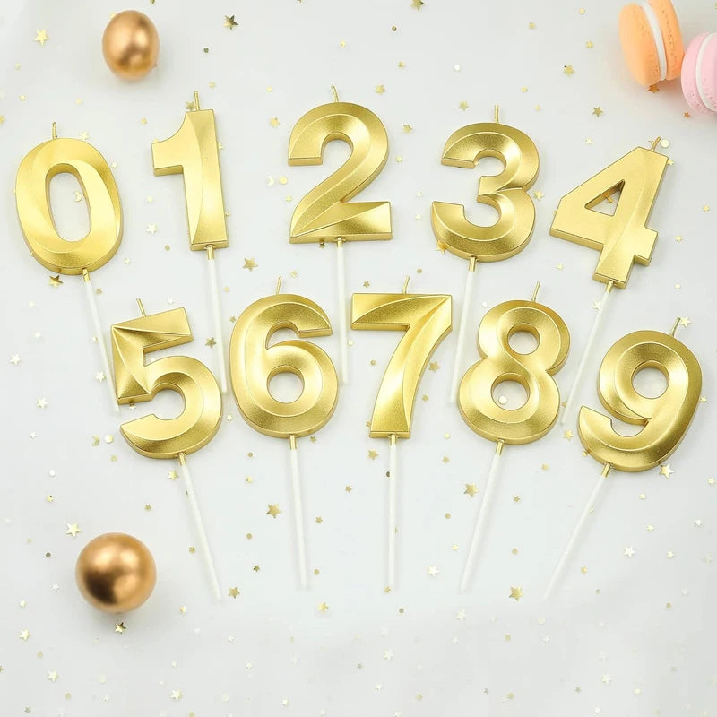 Gold numbered cake candles 0 through 9 arranged on a white surface with gold confetti and spherical decorations