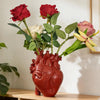 A bouquet of red and pink roses in a heart-shaped resin vase with gold accents