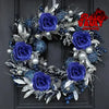 A dark floral wreath made of artificial purple and blue roses, silver foliage, and pearl accents.