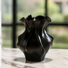 A dark, textured ceramic vase with a wave pattern sitting on a light marble surface.