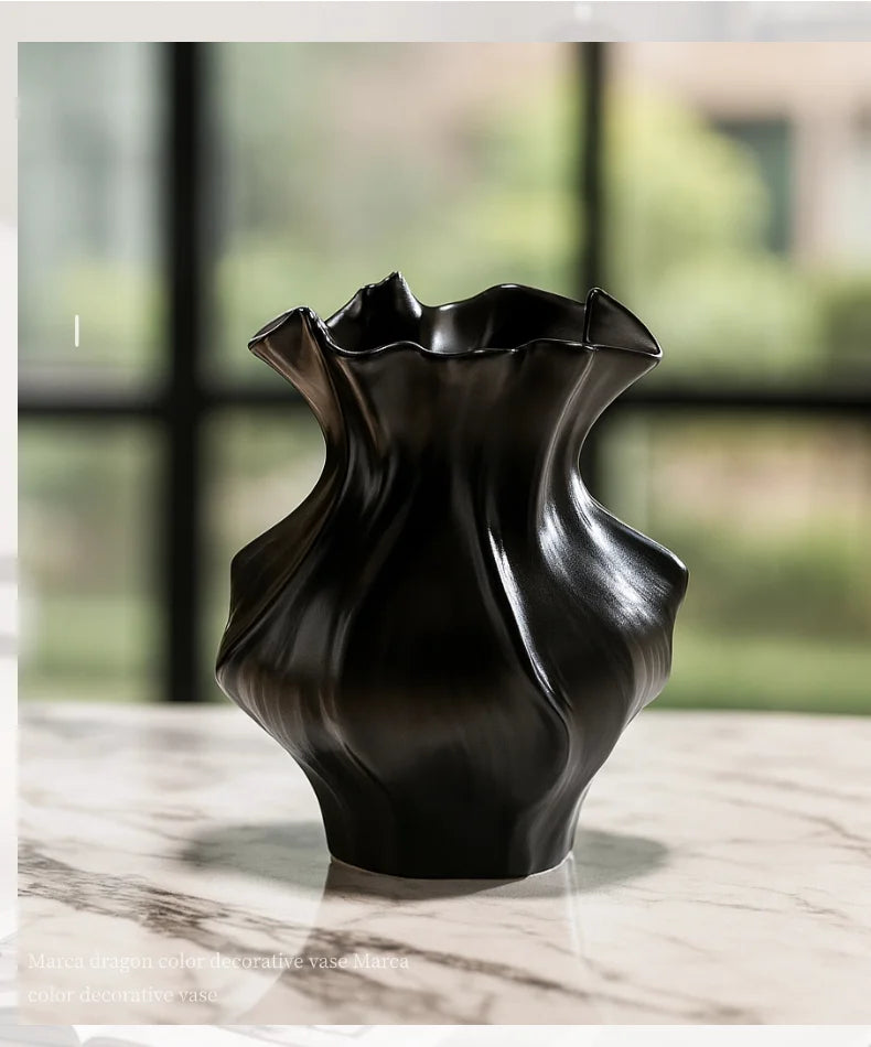 A dark, textured ceramic vase with a wave pattern sitting on a light marble surface.