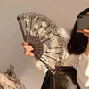 A hand holds an elegant black lace rose folding fan against a light background.