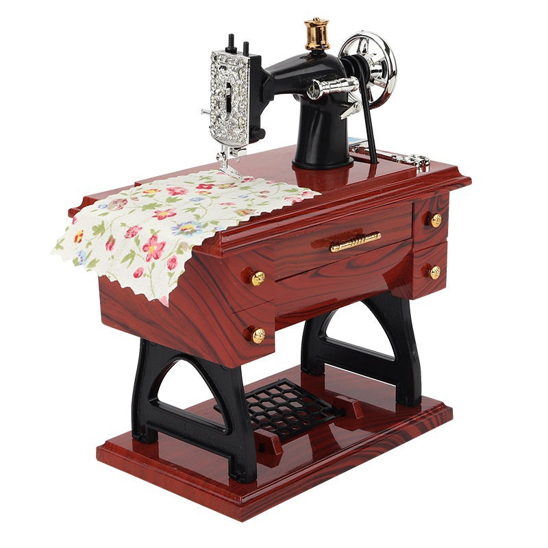 A vintage sewing machine music box with a brass crank and decorative silver accents sits on a wooden base.