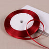 A roll of deep red satin ribbon on a white spool, resting on a light beige surface.