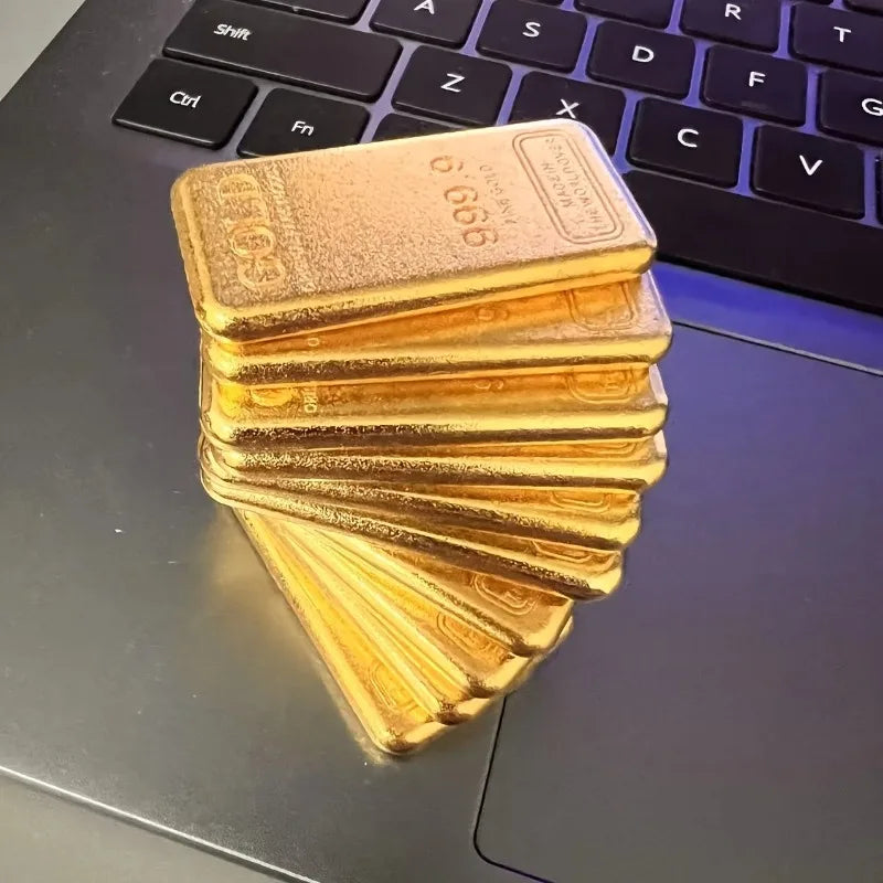 A stack of ten simulated gold ingot fortune charms resting on a dark laptop surface.