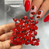 A hand displays a collection of red and black ladybug resin nail art charms in a clear plastic bag.