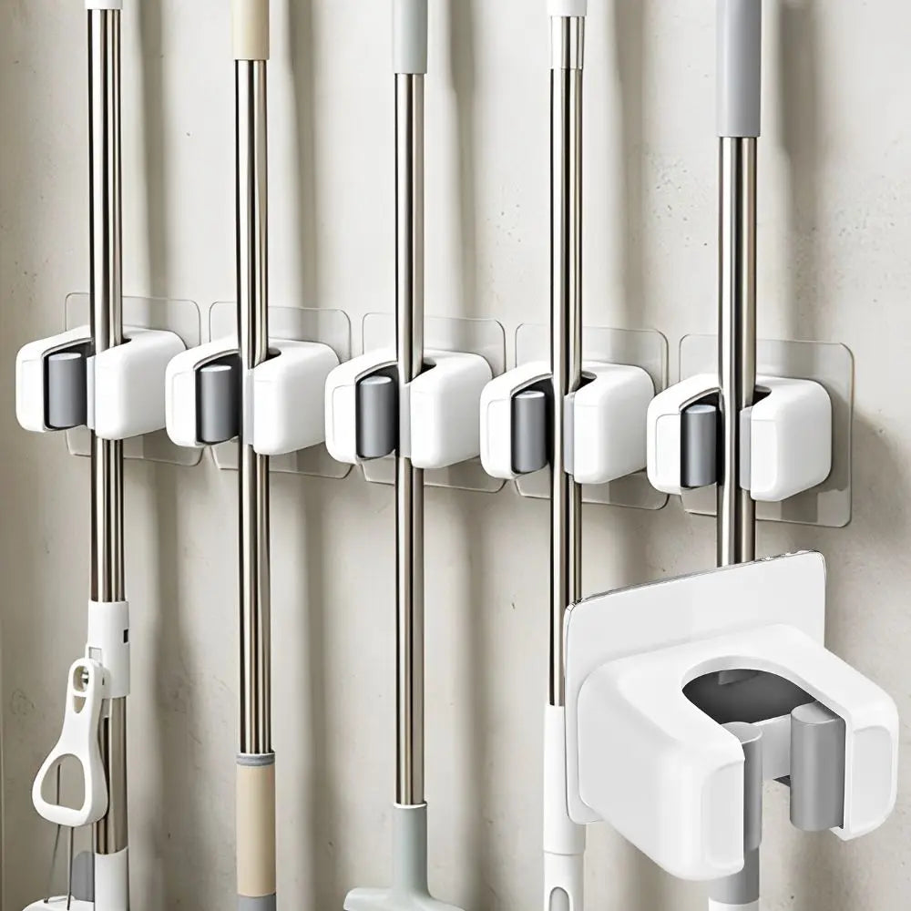 A set of three self-adhesive wall holders for mops, brooms, and long-handled tools mounted on a light-colored wall.