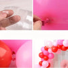 A close-up of a clear plastic double-hole balloon is being attached to a pink balloon, used for a balloon garland.
