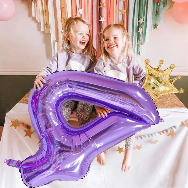 Two young girls smiling while holding a large purple foil number balloon shaped like the number 7.