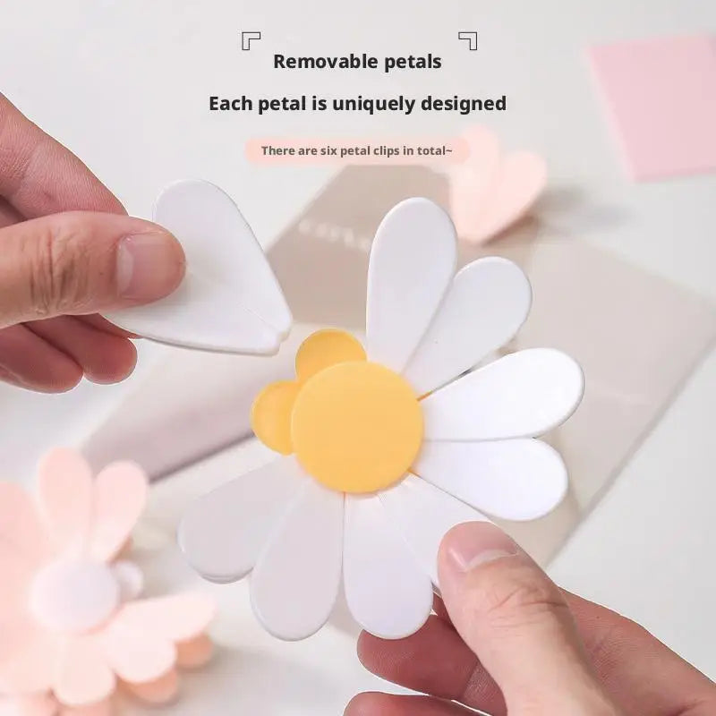 Mano sosteniendo una margarita blanca hecha de seis clips metálicos para sellar bolsas o decoración