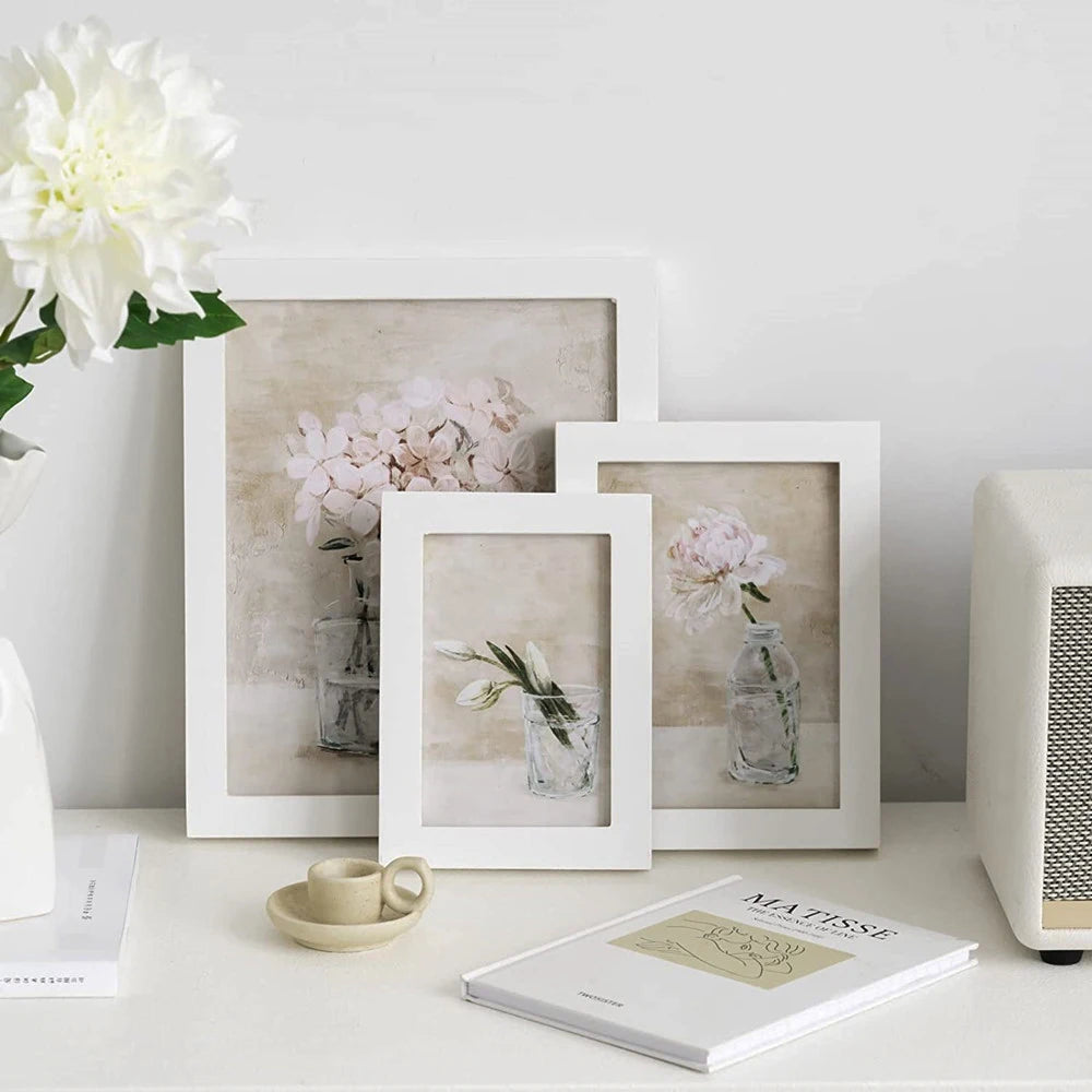 A natural wood picture frame with plexiglass displaying a pink floral arrangement on a white surface.