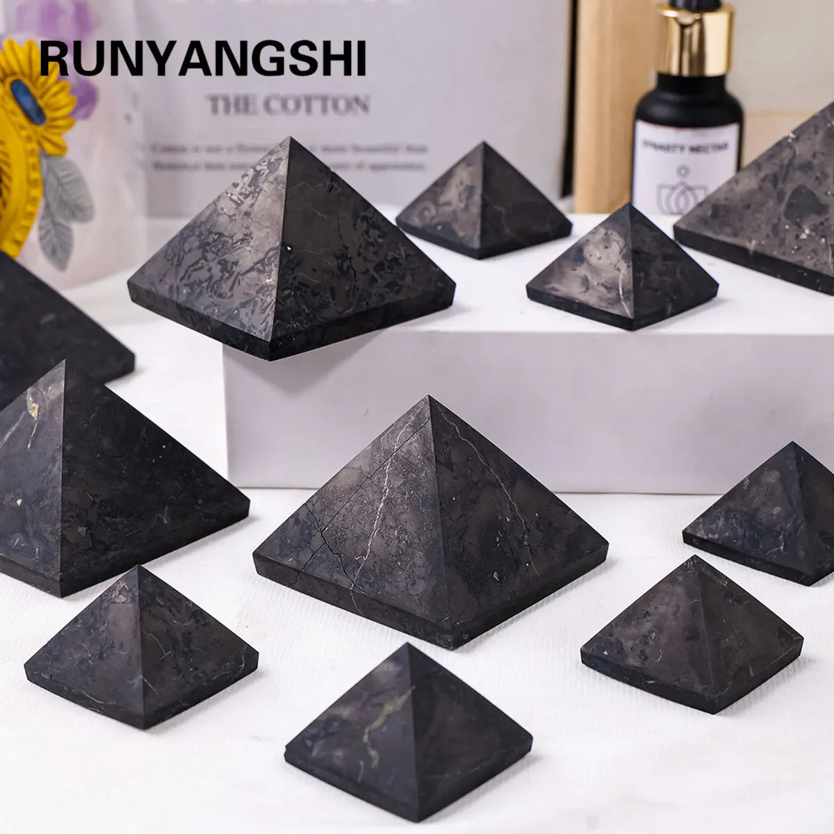 Una colección de pirámides de cristal de shungita gris oscuro expuestas sobre una superficie blanca.