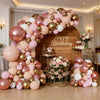 A large balloon garland featuring rose gold and pink balloons arranged in an archway against a wooden backdrop.
