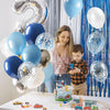 A young boy is interacting with a colorful balloon garland featuring blue, silver, and white balloons for a party.