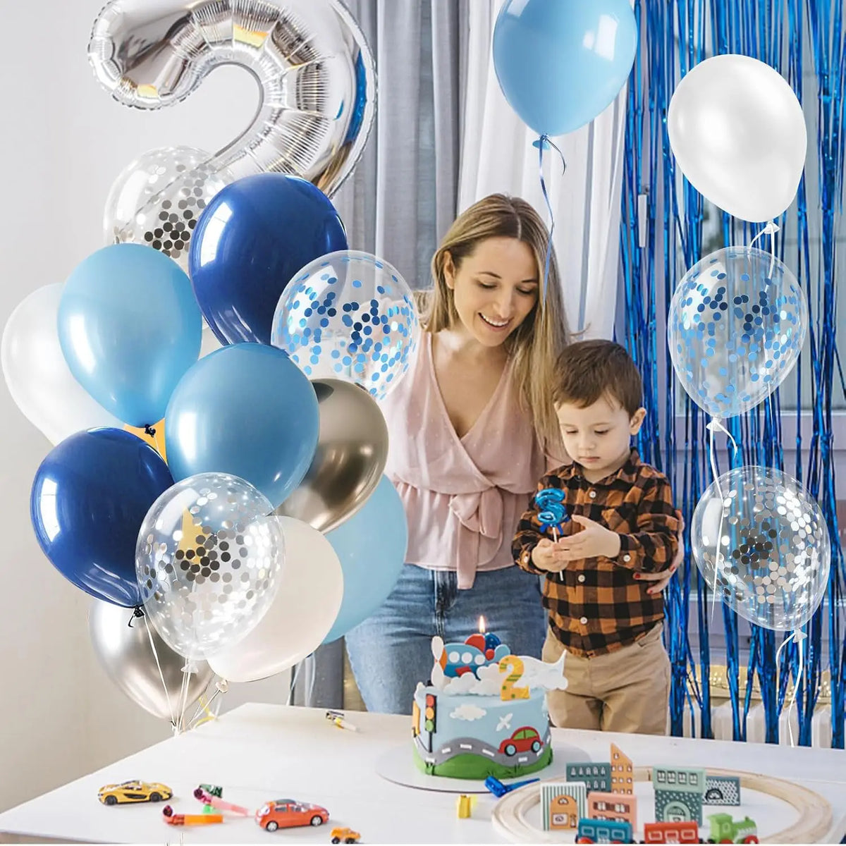 A young boy is interacting with a colorful balloon garland featuring blue, silver, and white balloons for a party.