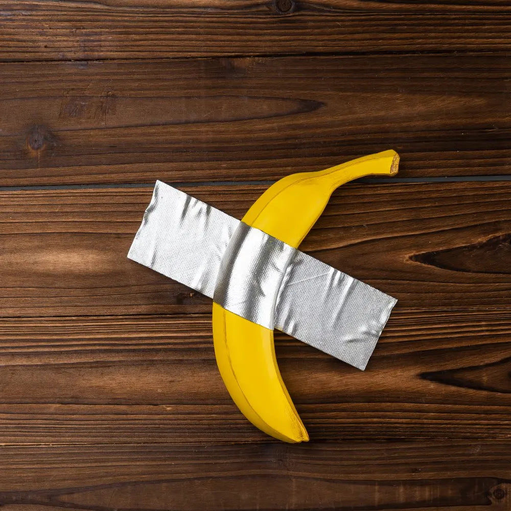 A yellow banana sculpture wrapped in silver fabric resting on a dark wooden surface.