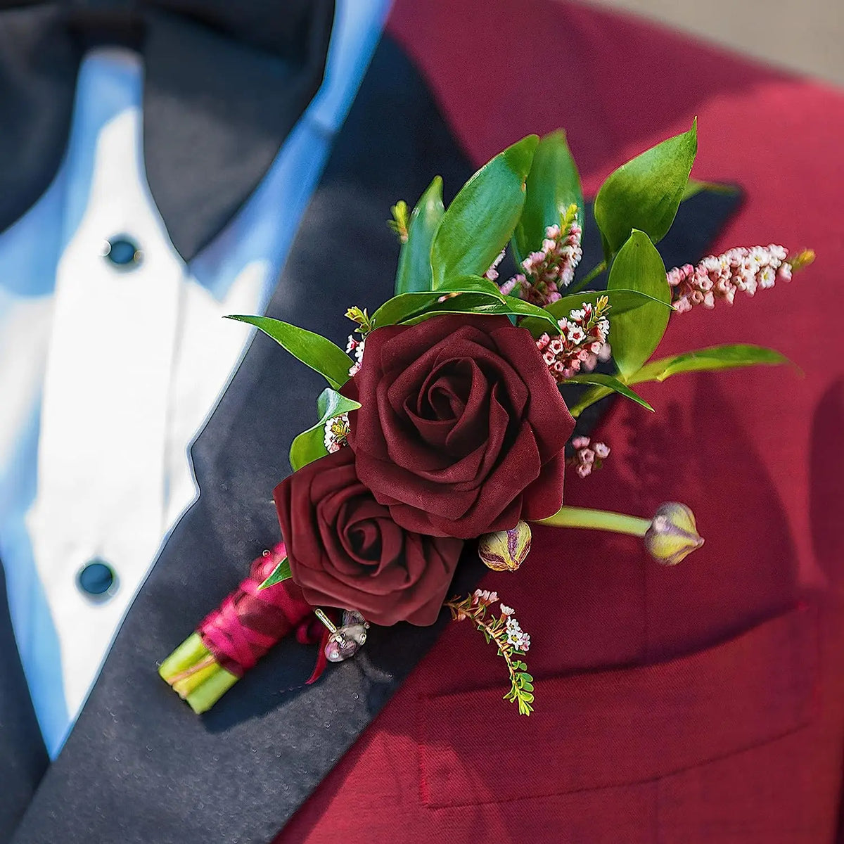 A bouquet of deep red artificial foam roses and green leaves arranged on a dark suit jacket.