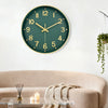 A modern silent quartz wall clock with a green face and gold accents hanging above a light beige sofa.
