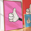 Arte de pared enmarcado en rosa con una mano blanca haciendo un pulgar arriba.