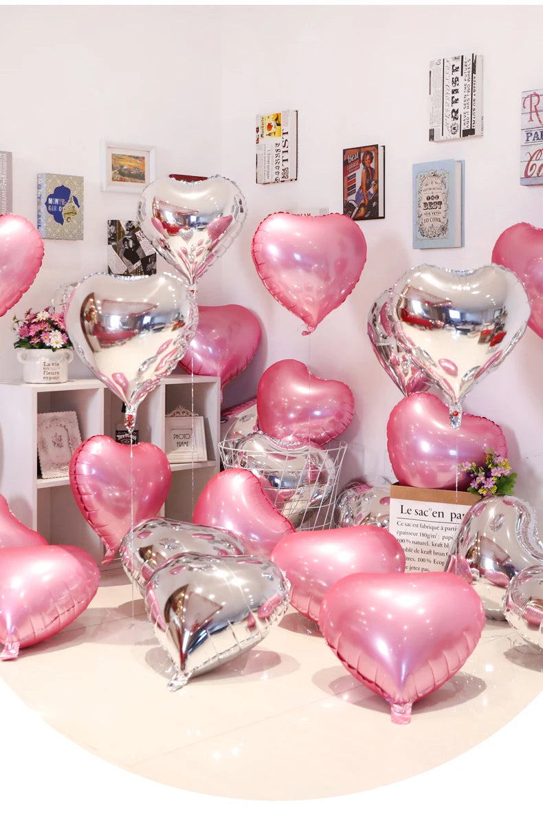 A collection of pink and silver heart foil balloons displayed against a white wall.
