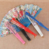 A collection of silk flower folding fans in various colors including pink, red, blue, and white, displayed on a beige fabric.