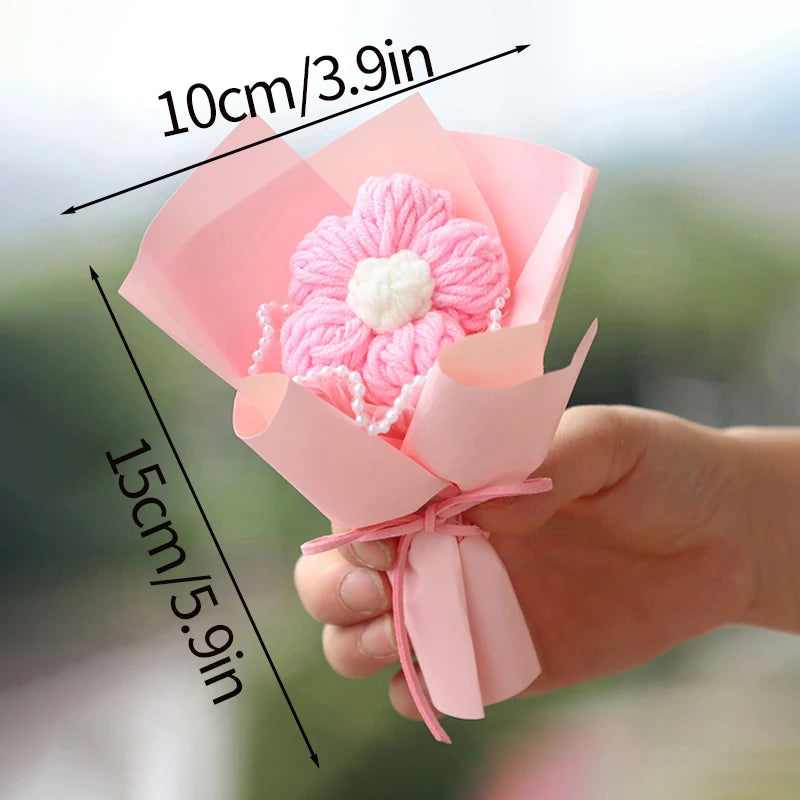 A pink handmade crochet flower bouquet with a white center is held in a hand.