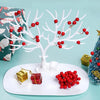 Una rama de árbol artificial blanca decorada con bayas de hieto rojo, mostrada en un plato blanco junto a una caja de regalo 
