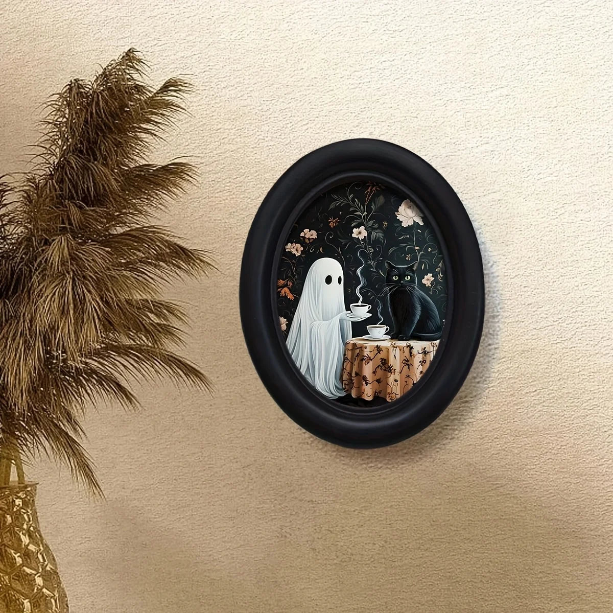 Oval framed wall art featuring a ghost, a black cat, and a teacup on a wooden surface.
