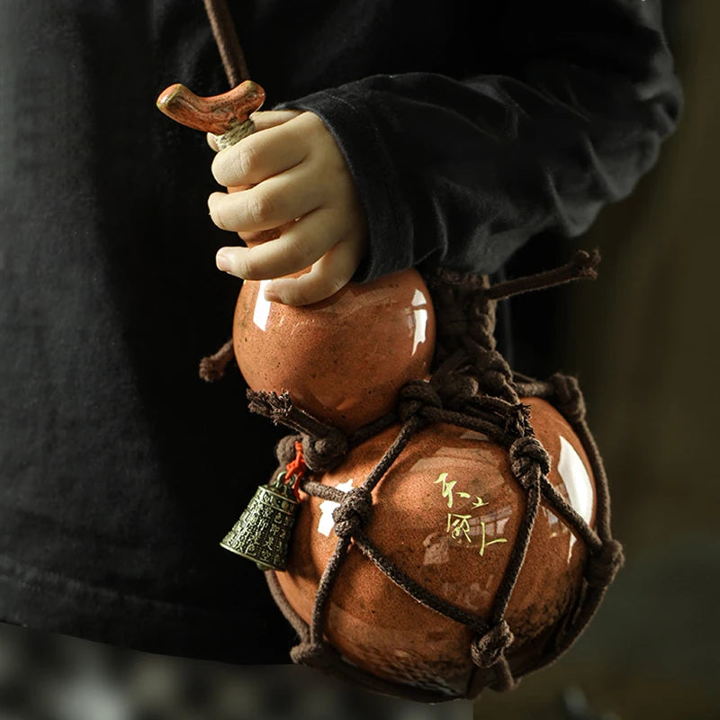 A hand holds a traditional ceramic wine gourd used for hot water and beverages.