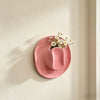 A pink ceramic cowboy hat shaped wall vase with white daisies mounted on a cream-colored wall.