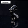 Figura de obsidiana negra y brillante con cabeza de animal estilizada, reflejando en una superficie oscura.