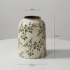 A rustic ceramic milk pitcher with a pale cream glaze and pastoral green floral design.