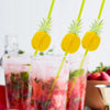 A glass of pink tropical drink garnished with a pineapple paper straw and flamingo paper straw.
