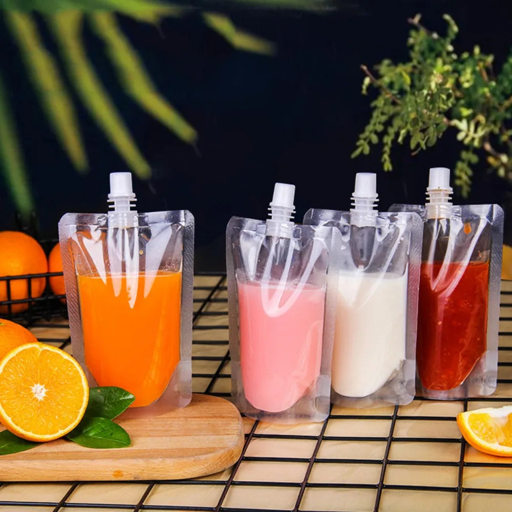 Several clear reusable pouches contain various colorful liquid drinks like orange juice, pink, and red juice on a wire rack.