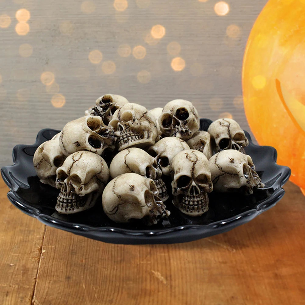 A pile of realistic skull figurines on a black plate with an orange pumpkin in the background.