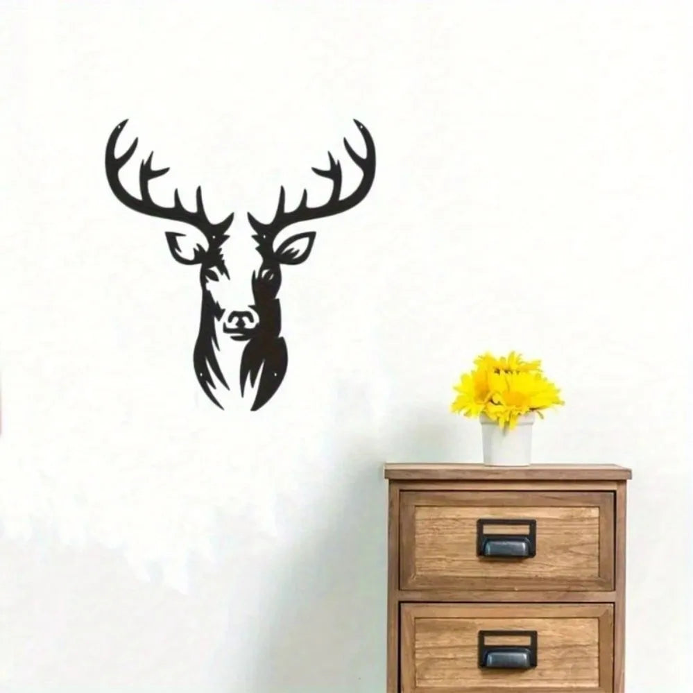 Black metal deer head wall sculpture with antlers mounted on a white wall above a wooden dresser.