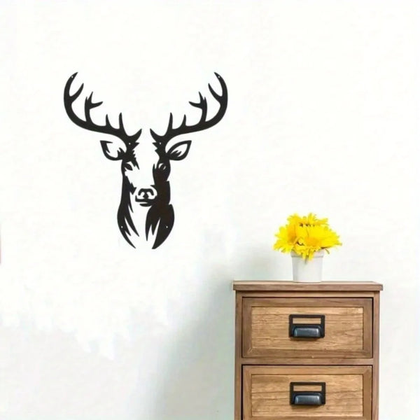 Black metal deer head wall sculpture with antlers mounted on a white wall above a wooden dresser.