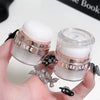 A hand holds two glass jars of Fairy Body Glitter Highlight Powder with white glitter inside.