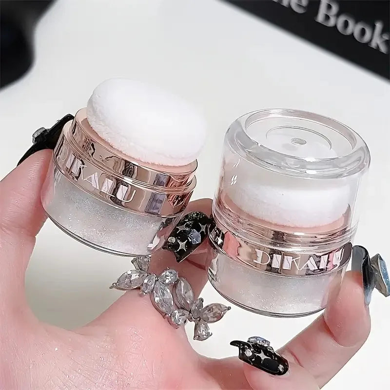A hand holds two glass jars of Fairy Body Glitter Highlight Powder with white glitter inside.
