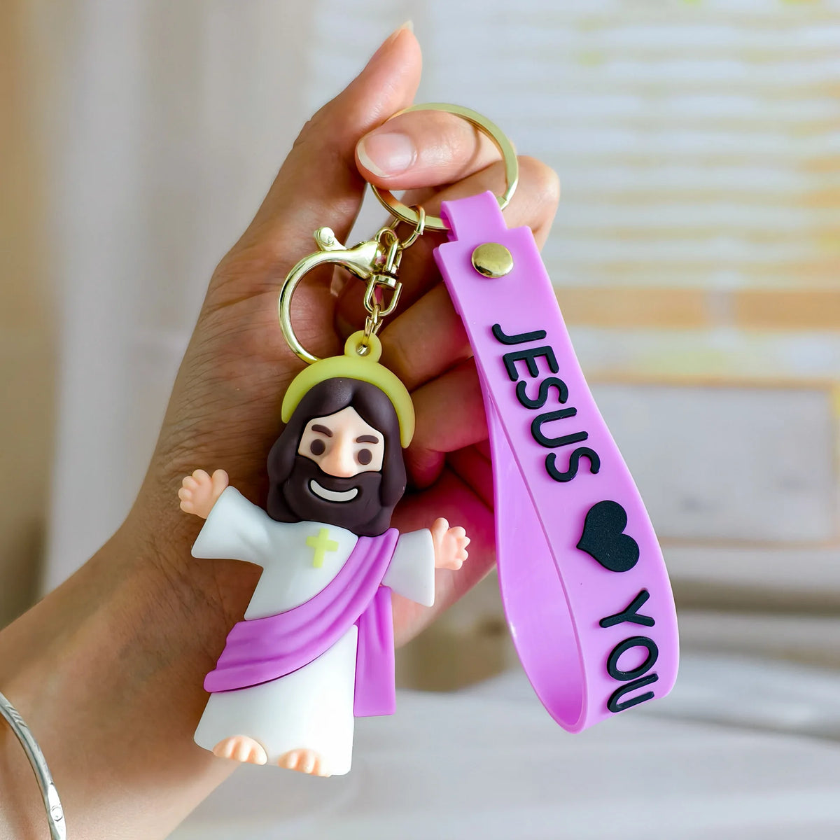 A hand holds a silicone keychain featuring a Jesus figure and a pink strap with the word Jesus you.