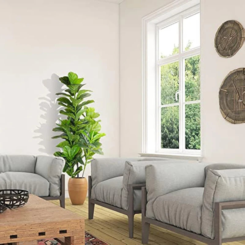 A potted artificial fiddle leaf fig tree in a terracotta pot sits on a wooden table next to a window.