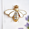 Gold resin animal wall hanging decor shaped like a bee mounted on a white wall.