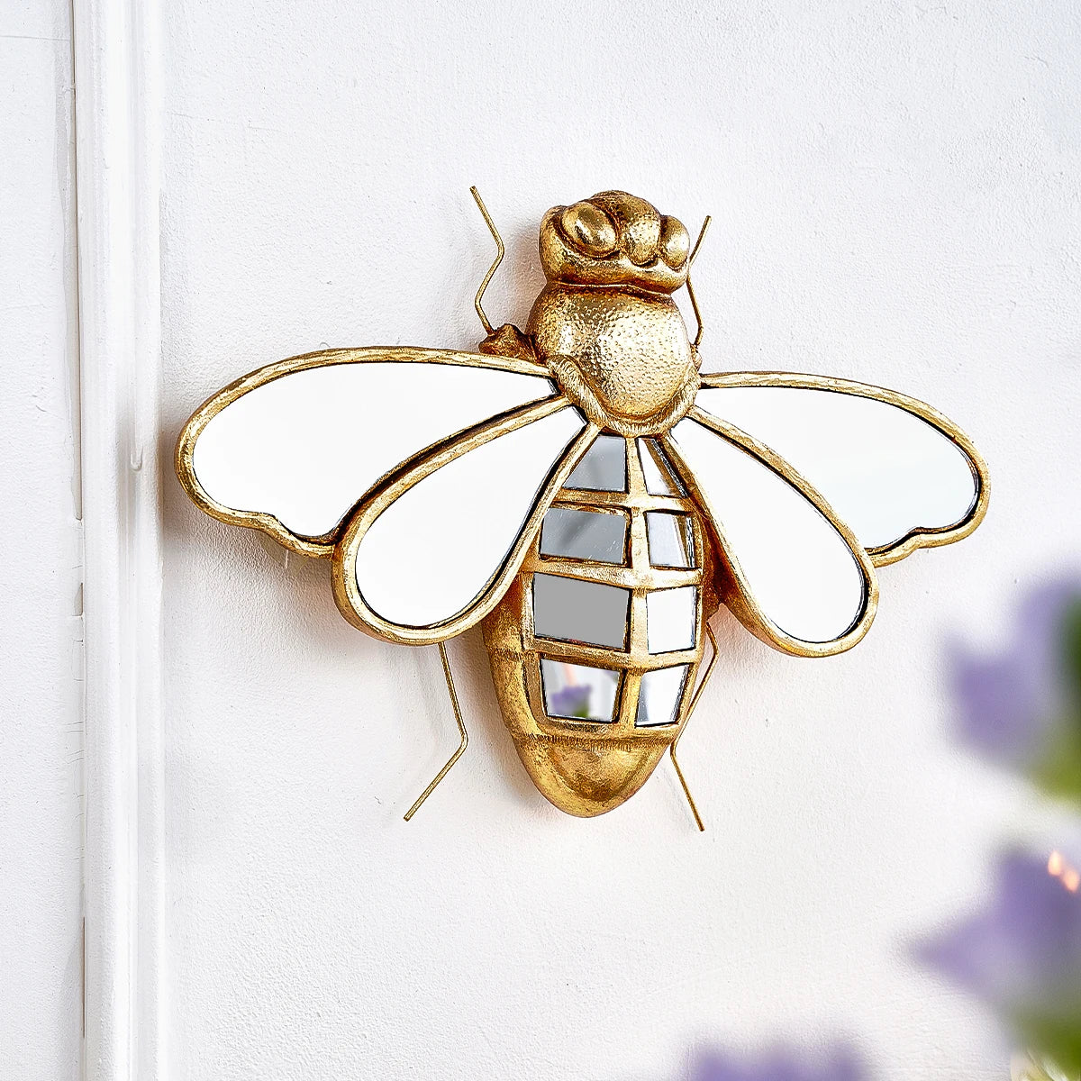Gold resin animal wall hanging decor shaped like a bee mounted on a white wall.