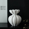 White ceramic vase with a fluted neck and rounded body displayed on a dark surface.