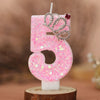 Pink glitter number five birthday candle with a silver crown topper on a wooden base