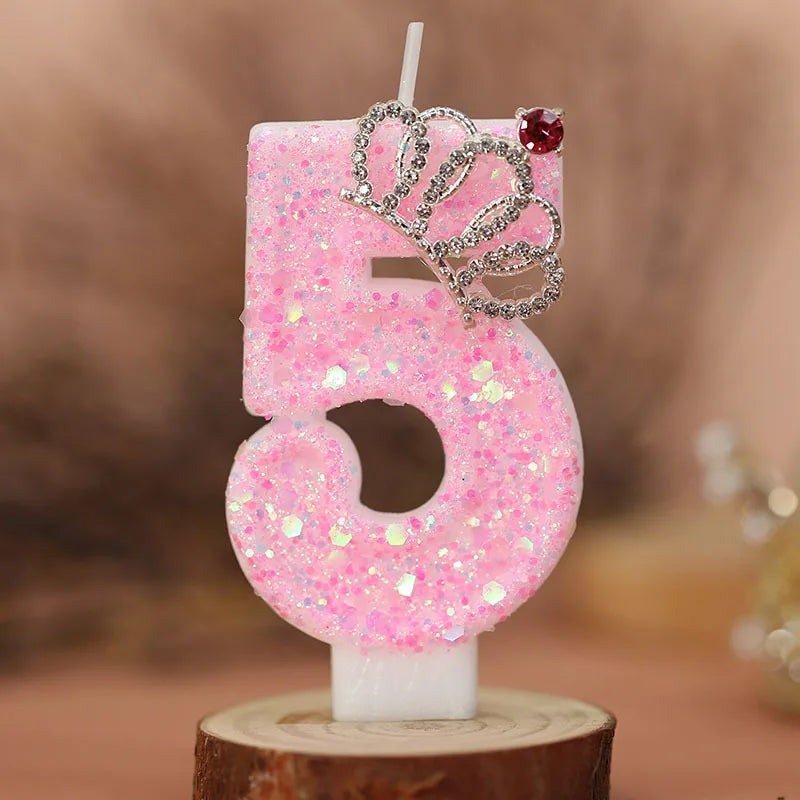 Pink glitter number five birthday candle with a silver crown topper on a wooden base