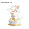 A white cake topper featuring a gold-edged hexagon with the text MELO BABY surrounded by dried floral elements.