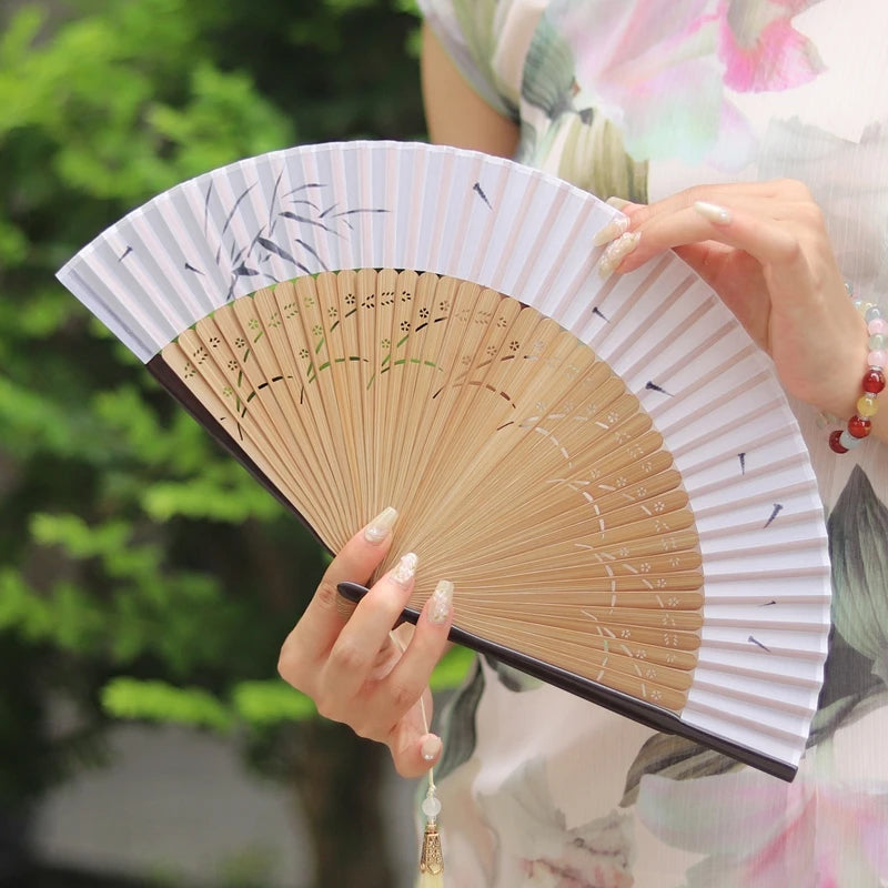A person holds an elegant bamboo folding fan with a white and gray striped cover and a tassel.