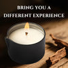 A black jar candle is lit, casting a warm glow on a wooden surface next to cinnamon sticks.